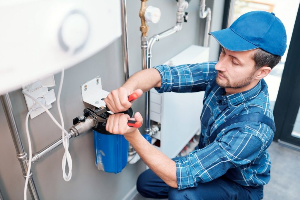 young man in workwear using pliers while installing water filtration system e1634566877708